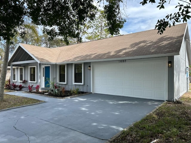 ranch-style home featuring concrete driveway, an attached garage, board and batten siding, and roof with shingles