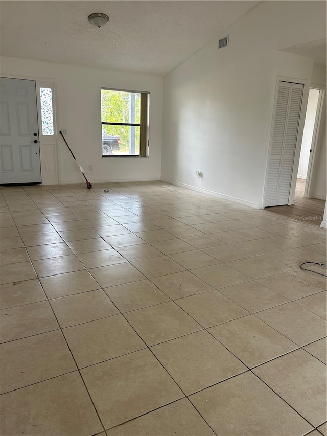 unfurnished room with a textured ceiling, baseboards, light tile patterned floors, lofted ceiling, and visible vents