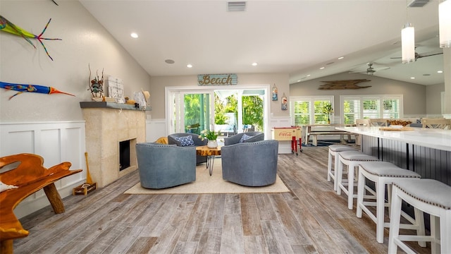 living room featuring visible vents, wainscoting, a decorative wall, light wood-type flooring, and vaulted ceiling