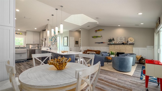 dining area with a decorative wall, wainscoting, lofted ceiling with skylight, and wood finished floors
