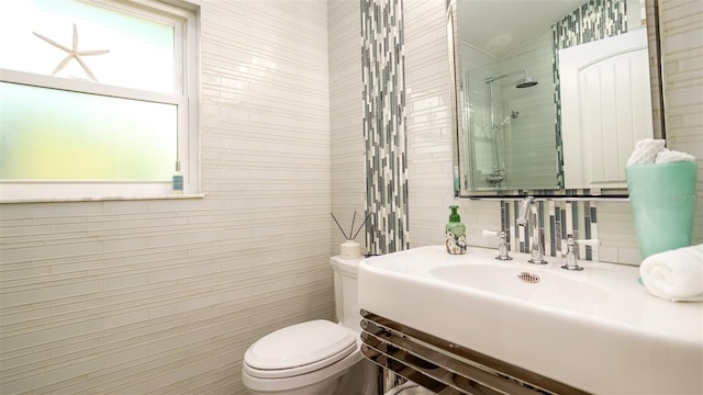 bathroom with a sink, toilet, tiled shower, and tile walls