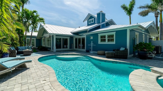 back of property with a standing seam roof, an outdoor living space, an outdoor pool, and a patio area