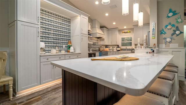 kitchen featuring custom range hood, dark wood-type flooring, a breakfast bar, and tasteful backsplash