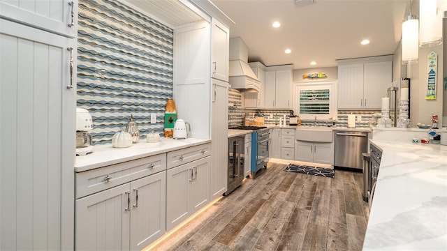 kitchen featuring a sink, stainless steel appliances, wood finished floors, custom exhaust hood, and backsplash