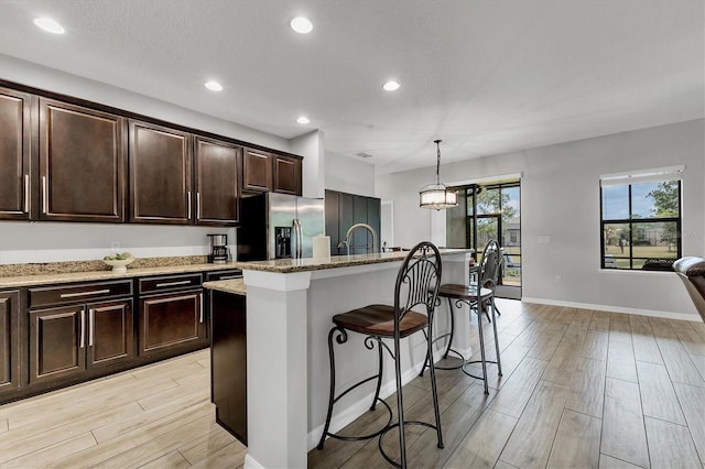 7418 61st St E, Palmetto, FL 34221 - kitchen with a breakfast bar area, light stone countertops, light wood finished floors, and stainless steel fridge with ice dispenser