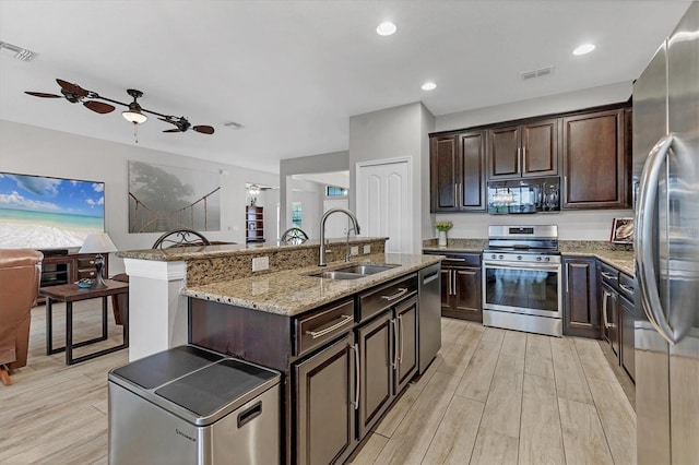 7418 61st St E, Palmetto, FL 34221 - kitchen with stainless steel appliances, an island with sink, a sink, and light wood-style flooring