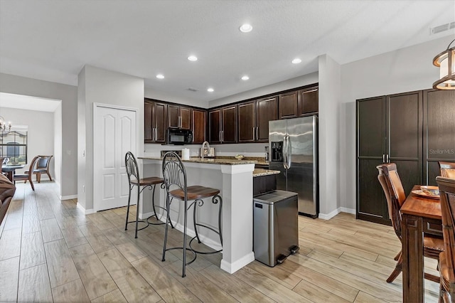 7418 61st St E, Palmetto, FL 34221 - kitchen featuring dark brown cabinetry, black microwave, stainless steel fridge, visible vents, and a center island with sink