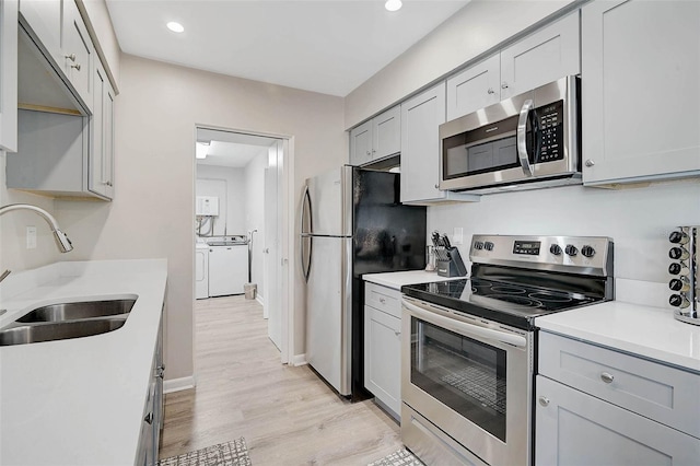 1112 65th St NW, Bradenton, FL 34209 - kitchen featuring washing machine and dryer, light countertops, a sink, light wood-style flooring, and appliances with stainless steel finishes