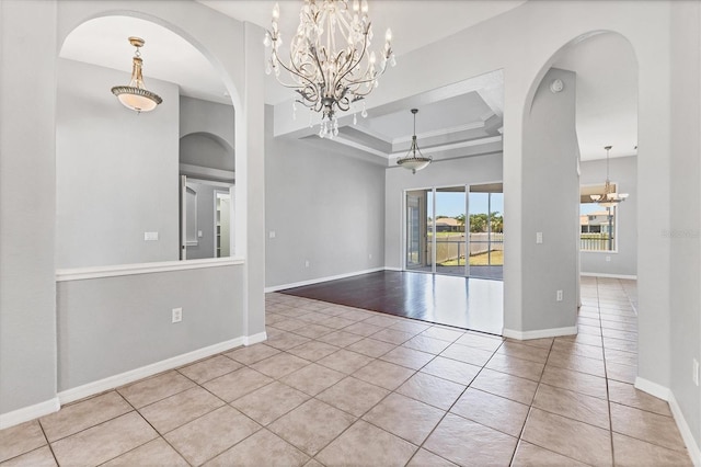 tiled empty room with a notable chandelier, baseboards, a raised ceiling, arched walkways, and ornamental molding