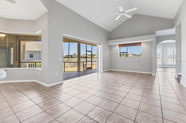 tiled empty room with arched walkways, ceiling fan, baseboards, and high vaulted ceiling