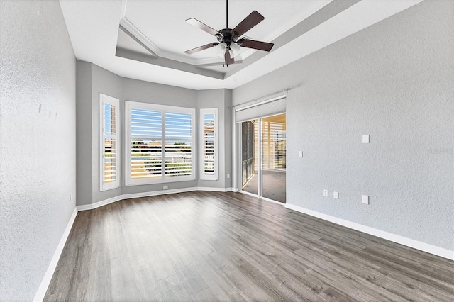 spare room featuring wood finished floors, a tray ceiling, baseboards, ceiling fan, and a textured wall