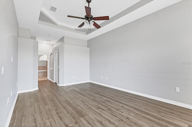 spare room featuring wood finished floors, visible vents, a ceiling fan, a raised ceiling, and baseboards