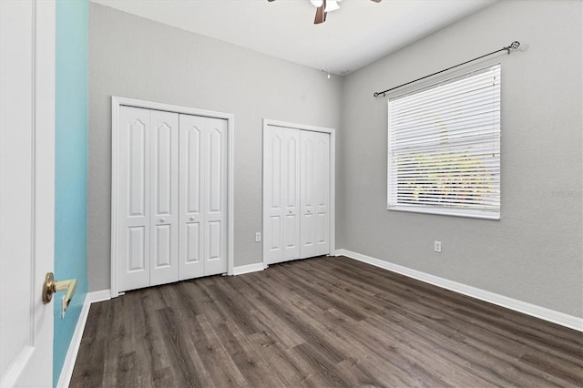 unfurnished bedroom with baseboards, dark wood-style flooring, ceiling fan, and two closets