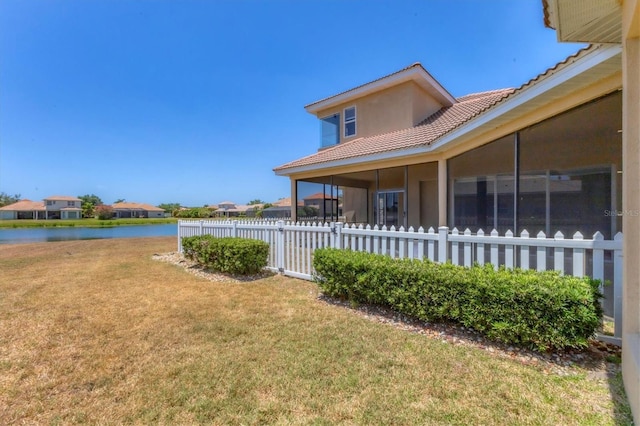 exterior space with a tile roof, a yard, stucco siding, a sunroom, and a water view