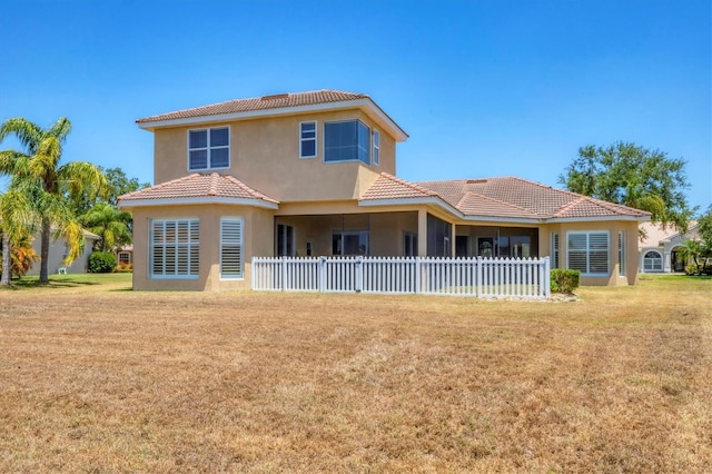 rear view of property with a yard, stucco siding, a tile roof, and fence