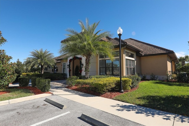view of front of property with stucco siding, a tiled roof, a front lawn, and uncovered parking