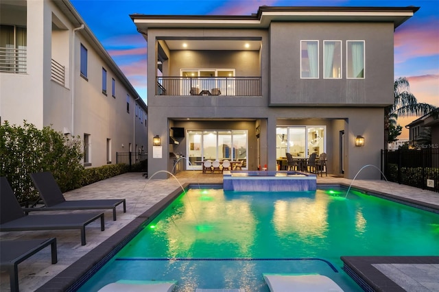 1514 Corolla Ct, Reunion, FL 34747 - back of house at dusk featuring a balcony, a pool with connected hot tub, a patio area, fence, and stucco siding