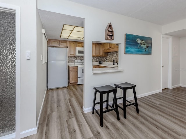 340 Base Ave E Unit 314, Venice, FL 34285 - kitchen featuring a kitchen breakfast bar, brown cabinetry, light wood-type flooring, light countertops, and white appliances