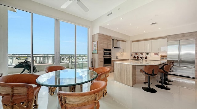 kitchen with appliances with stainless steel finishes, modern cabinets, wall chimney range hood, a kitchen breakfast bar, and healthy amount of natural light