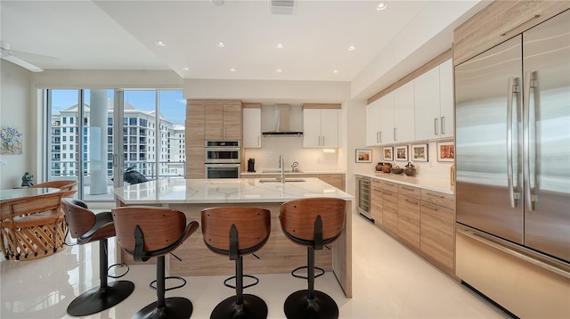 kitchen with appliances with stainless steel finishes, wall chimney exhaust hood, wine cooler, modern cabinets, and a breakfast bar
