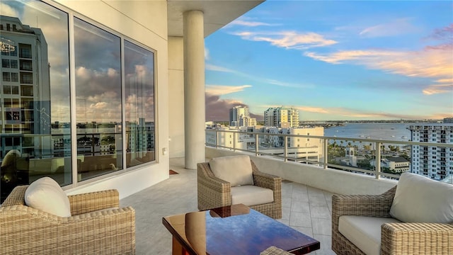 balcony at dusk featuring a water view and a city view