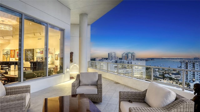 balcony at dusk featuring a view of city and a water view