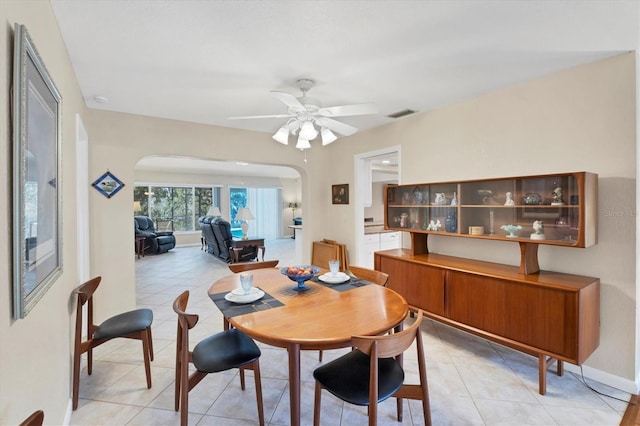dining room featuring arched walkways, ceiling fan, light tile patterned floors, and baseboards