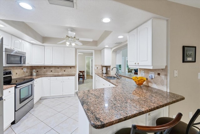 kitchen with appliances with stainless steel finishes, a sink, a breakfast bar area, a tray ceiling, and a peninsula
