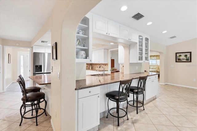 kitchen featuring stainless steel fridge, a sink, a kitchen breakfast bar, arched walkways, and glass insert cabinets