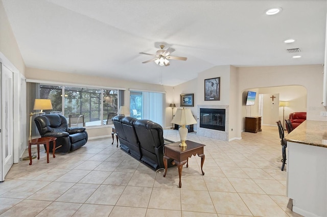 living room with vaulted ceiling, a ceiling fan, light tile patterned floors, a tiled fireplace, and baseboards