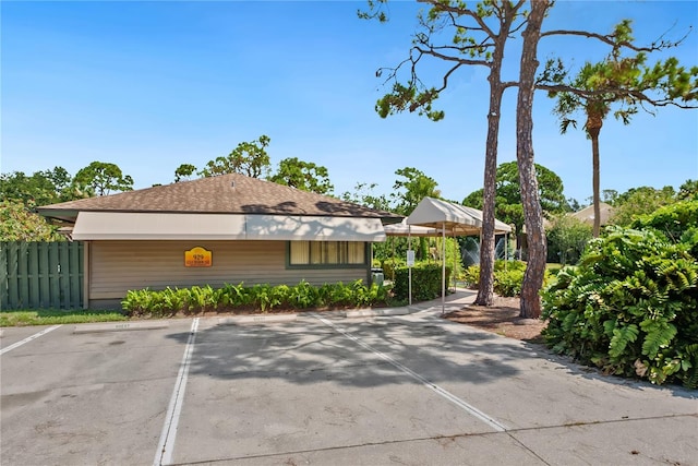 exterior space with fence, uncovered parking, and a shingled roof
