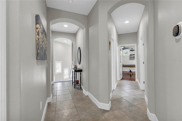 hall featuring arched walkways, baseboards, and plenty of natural light