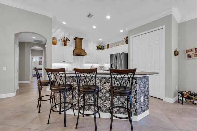 kitchen featuring visible vents, stainless steel fridge with ice dispenser, premium range hood, white cabinetry, and vaulted ceiling