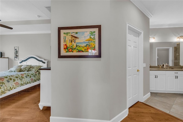 bedroom featuring crown molding, light wood-type flooring, a sink, baseboards, and connected bathroom