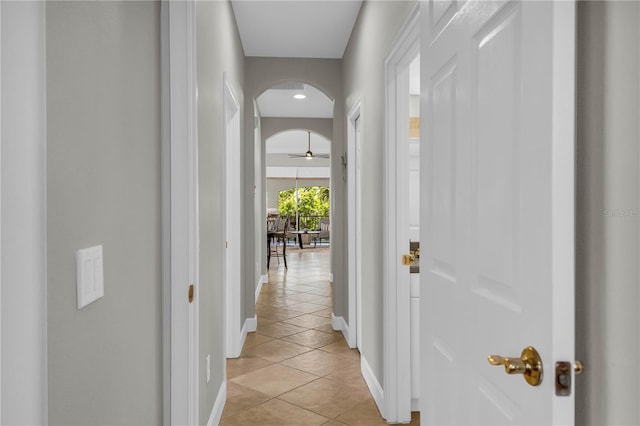 hallway featuring baseboards, arched walkways, and light tile patterned floors
