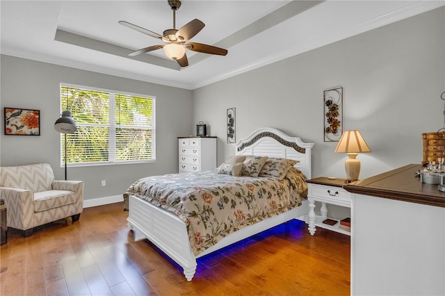 bedroom with ornamental molding, wood finished floors, baseboards, a raised ceiling, and a ceiling fan