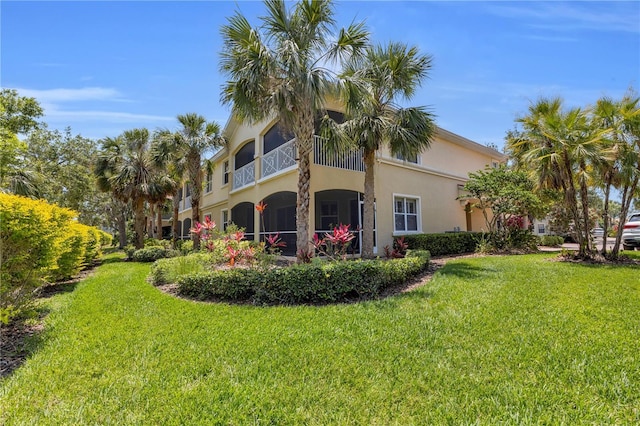 back of house featuring a lawn, stucco siding, and a balcony