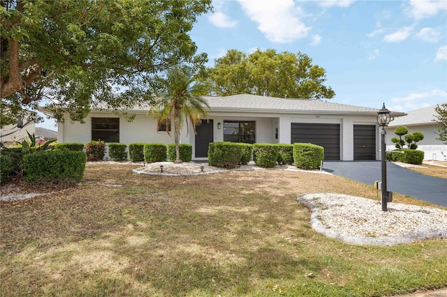 single story home featuring a garage, a front lawn, aphalt driveway, and stucco siding