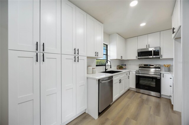kitchen featuring a sink, light wood-style floors, light countertops, stainless steel appliances, and decorative backsplash