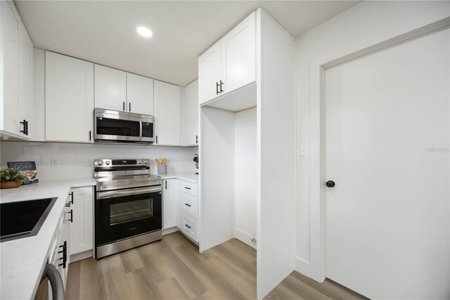kitchen with backsplash, light countertops, light wood finished floors, stainless steel appliances, and white cabinetry