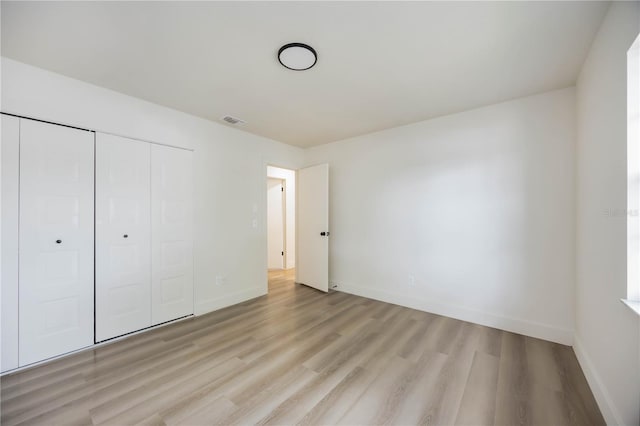 unfurnished bedroom featuring baseboards, visible vents, light wood finished floors, and a closet