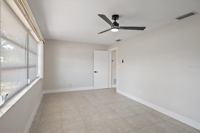 empty room featuring a textured ceiling, ceiling fan, visible vents, and light tile patterned floors