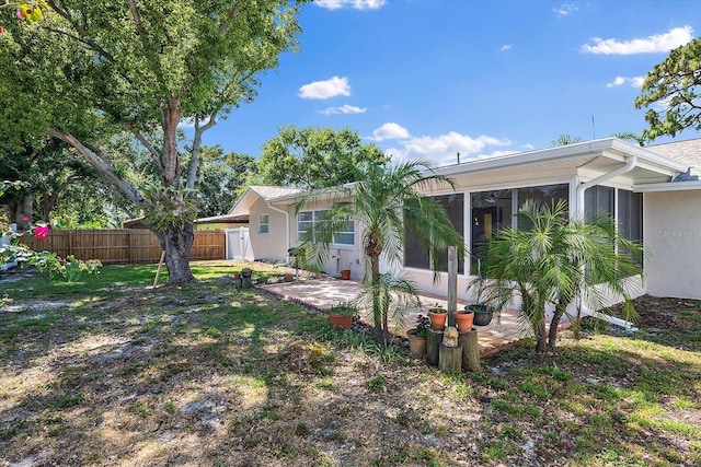rear view of property featuring fence, stucco siding, a sunroom, and a patio area