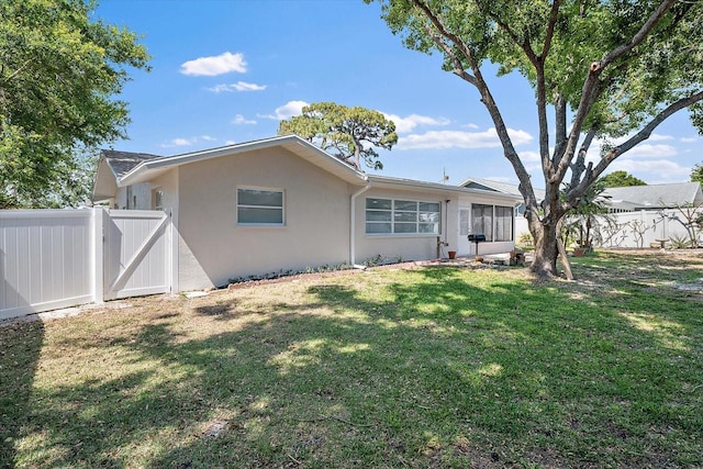 back of house with a lawn, fence, a gate, and stucco siding