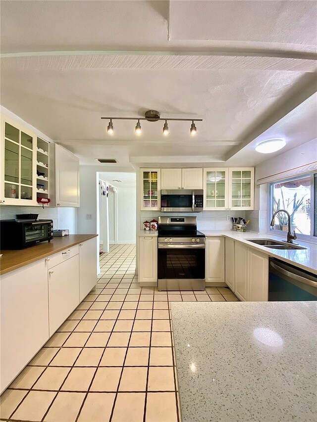 kitchen with a toaster, glass insert cabinets, a sink, light tile patterned floors, and stainless steel appliances
