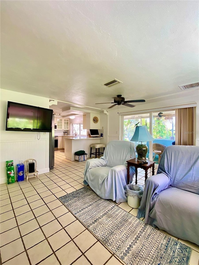 living room with a textured ceiling, a ceiling fan, light tile patterned flooring, and visible vents