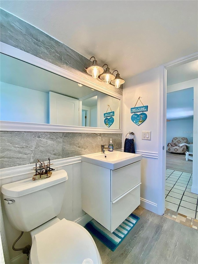 bathroom with a wainscoted wall, toilet, wood finished floors, and vanity