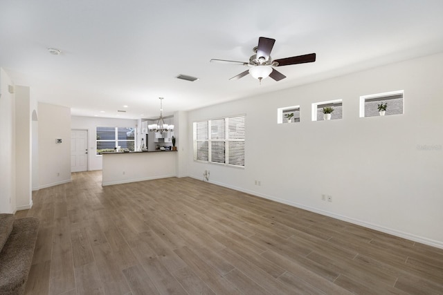 unfurnished living room with plenty of natural light, ceiling fan with notable chandelier, and wood finished floors