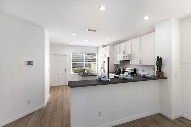 kitchen featuring white cabinets, dark countertops, light wood finished floors, stainless steel appliances, and a peninsula