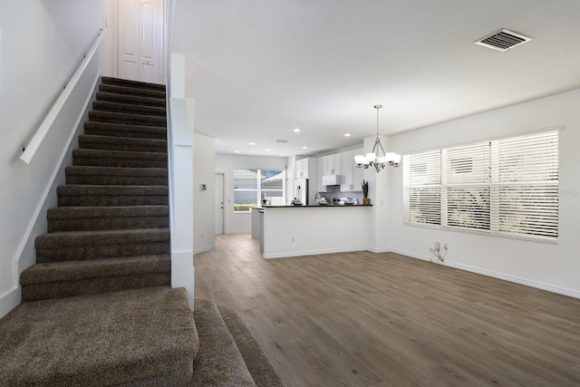 unfurnished living room featuring a notable chandelier, recessed lighting, wood finished floors, visible vents, and stairway
